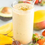 Mango smoothie in a glass with strawberries, avocado and dates around it