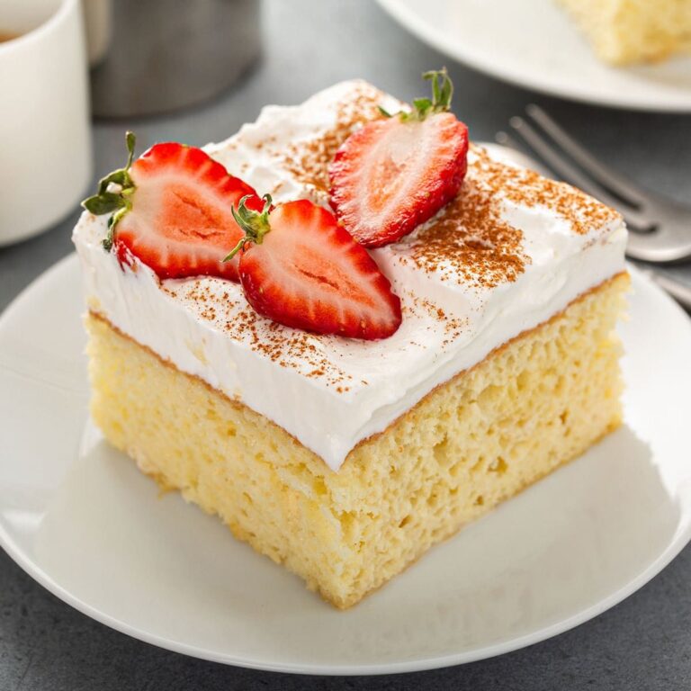 Slices of tres leches cake topped with whipped cream and strawberries