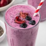 Purple berry smoothie topped with blueberries and cherries, with a striped straw