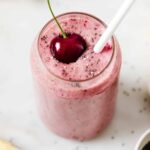 Cherry vanilla smoothie in a glass jar topped with a fresh cherry and a straw