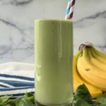 Green anti-stress smoothie in a tall glass with a striped straw