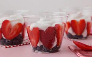 Clear cups of blueberries and yogurt with heart-shaped strawberry slices pressed against the sides