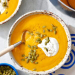 Bowl of carrot ginger soup topped with yogurt and pumpkin seeds