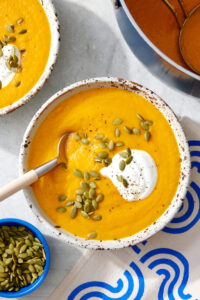Bowl of carrot ginger soup topped with yogurt and pumpkin seeds
