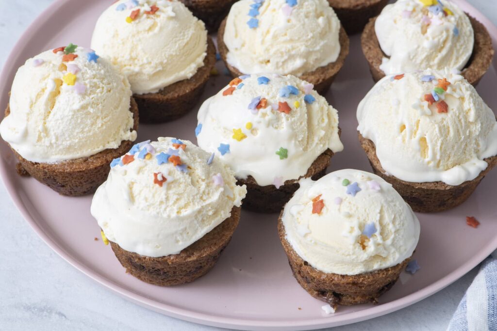 Chocolate chip cookie cups filled with scoops of vanilla ice cream and sprinkles on a pink plate