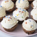 Chocolate chip cookie cups filled with scoops of vanilla ice cream and sprinkles on a pink plate