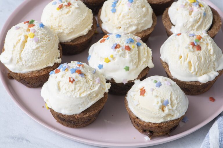 Chocolate chip cookie cups filled with scoops of vanilla ice cream and sprinkles on a pink plate