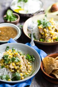 Bowls of crock pot chicken chili verde with corn over rice, with tortilla chips