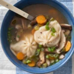 Bowl of dumpling soup with shiitake mushrooms, carrots and scallions