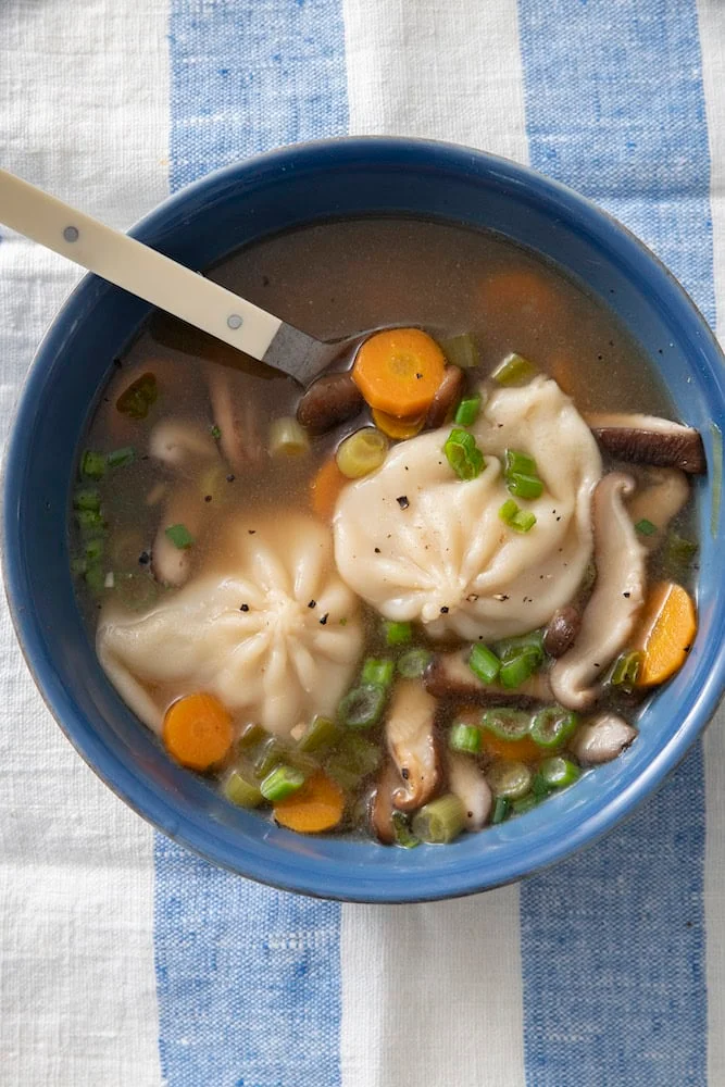 Bowl of dumpling soup with shiitake mushrooms, carrots and scallions