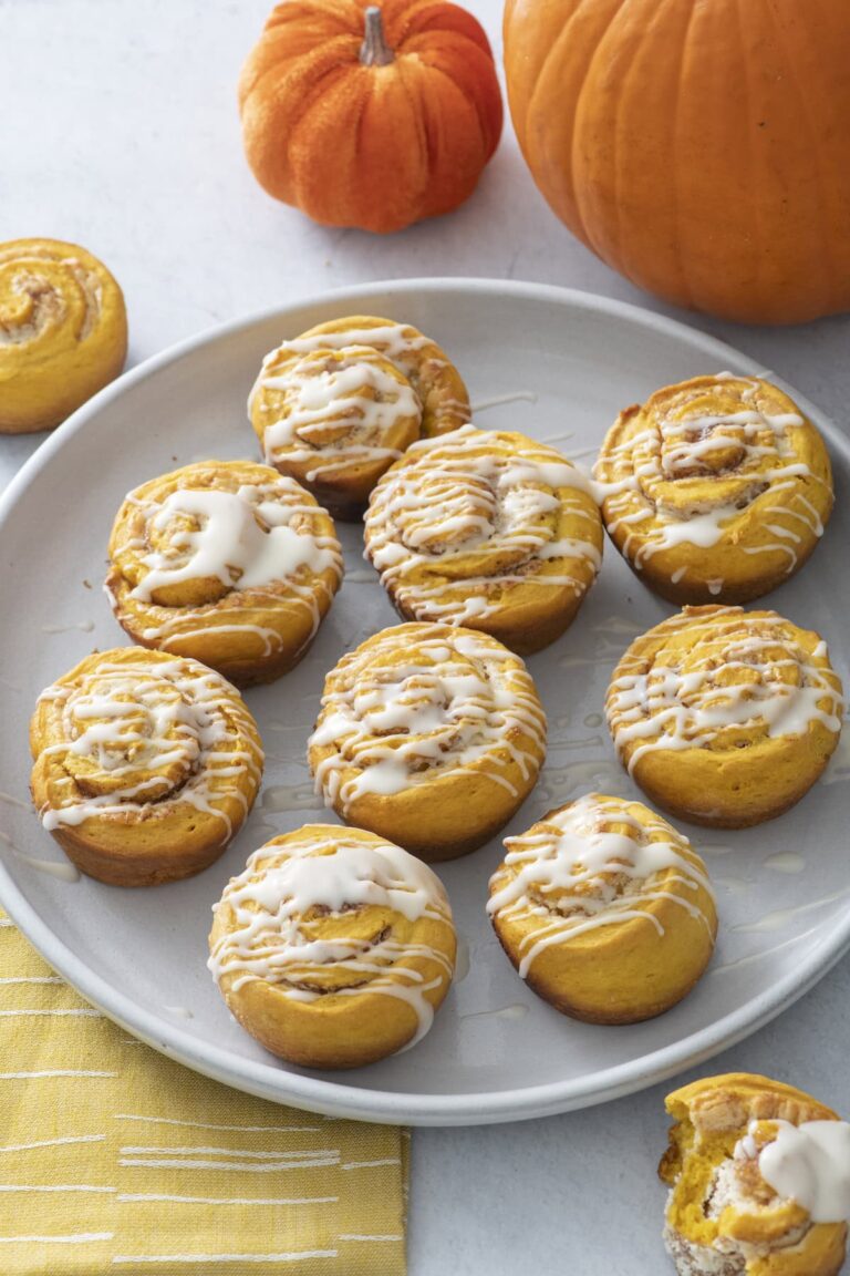 Glazed pumpkin cinnamon rolls on a plate next to small pumpkins