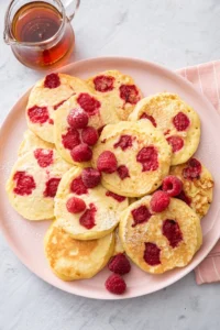 Raspberry pancakes on a pink plate with syrup