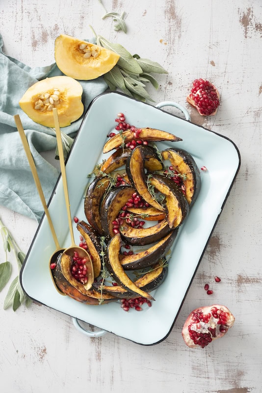 Roasted acorn squash slices with pomegranate seeds on a platter