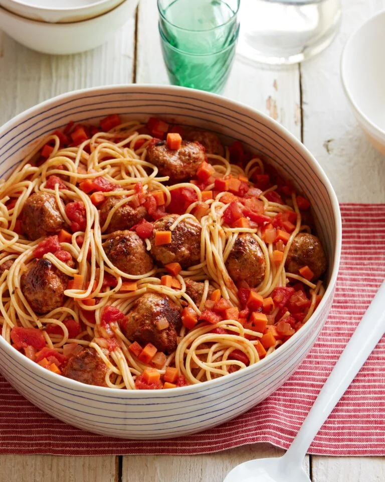 Spaghetti with turkey meatballs in a chunky tomato and carrot sauce in a striped serving bowl