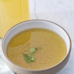 Bowl of golden bone broth with a jar behind