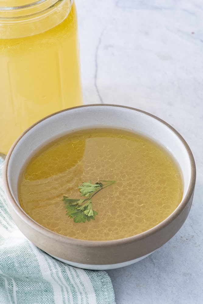 Bowl of golden bone broth with a jar behind
