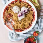 Strawberry rhubarb crumble in a baking dish topped with scoops of ice cream, with fresh strawberries