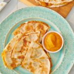 Sweet pumpkin quesadilla wedges on a plate with a small bowl of pumpkin purée