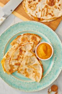 Sweet pumpkin quesadilla wedges on a plate with a small bowl of pumpkin purée