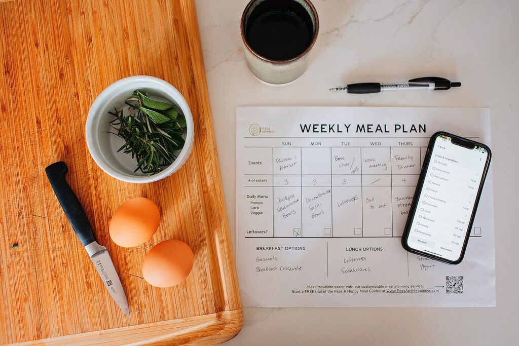 Weekly meal plan sheet, phone, eggs and herbs on a cutting board