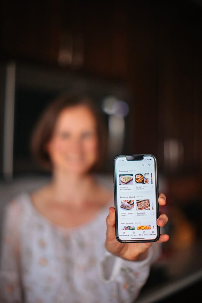Ann Kent holding a phone showing the Peas & Hoppiness meal planning app