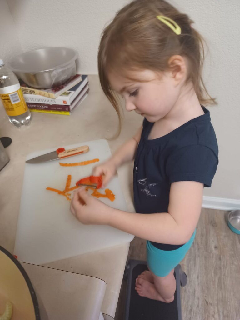 A young girl slicing carrots at the kitchen counter