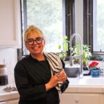 Chef Candice, a latina woman in her mid-30s, smiles directly at the camera. She stands in a white kitchen.