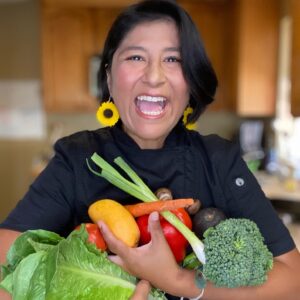 Chef Carmen Karlsgodt laughing with an armful of fresh vegetables