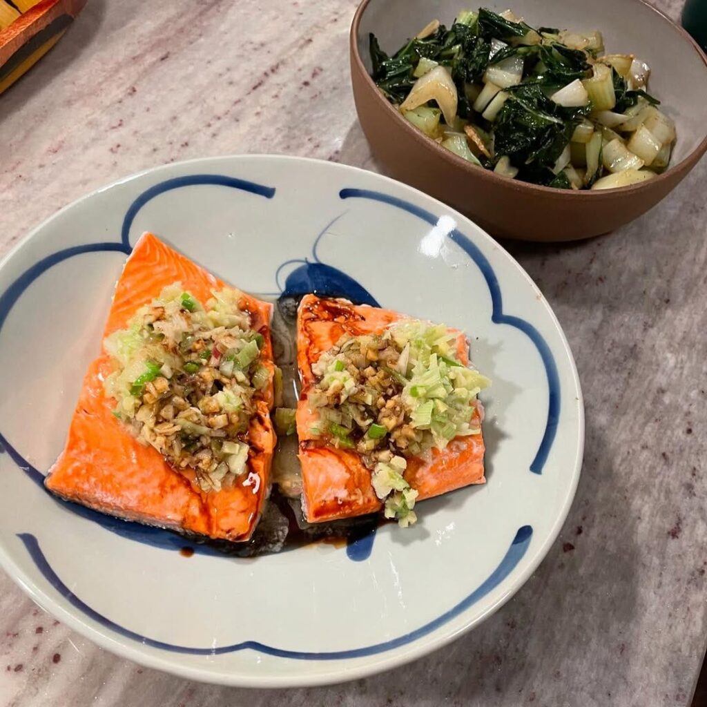 Two pieces of glazed salmon topped with scallion relish, with a bowl of greens