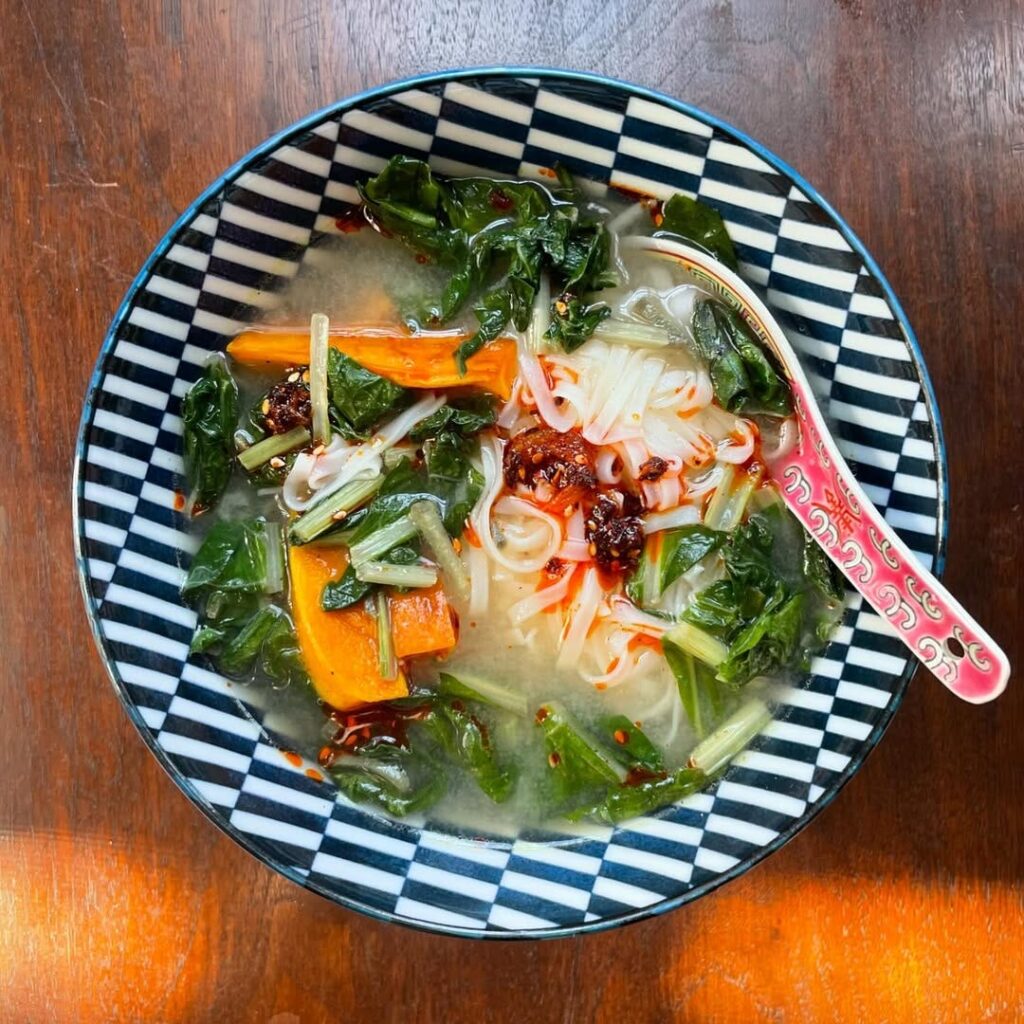 Bowl of rice noodle soup with greens, squash and chili crisp