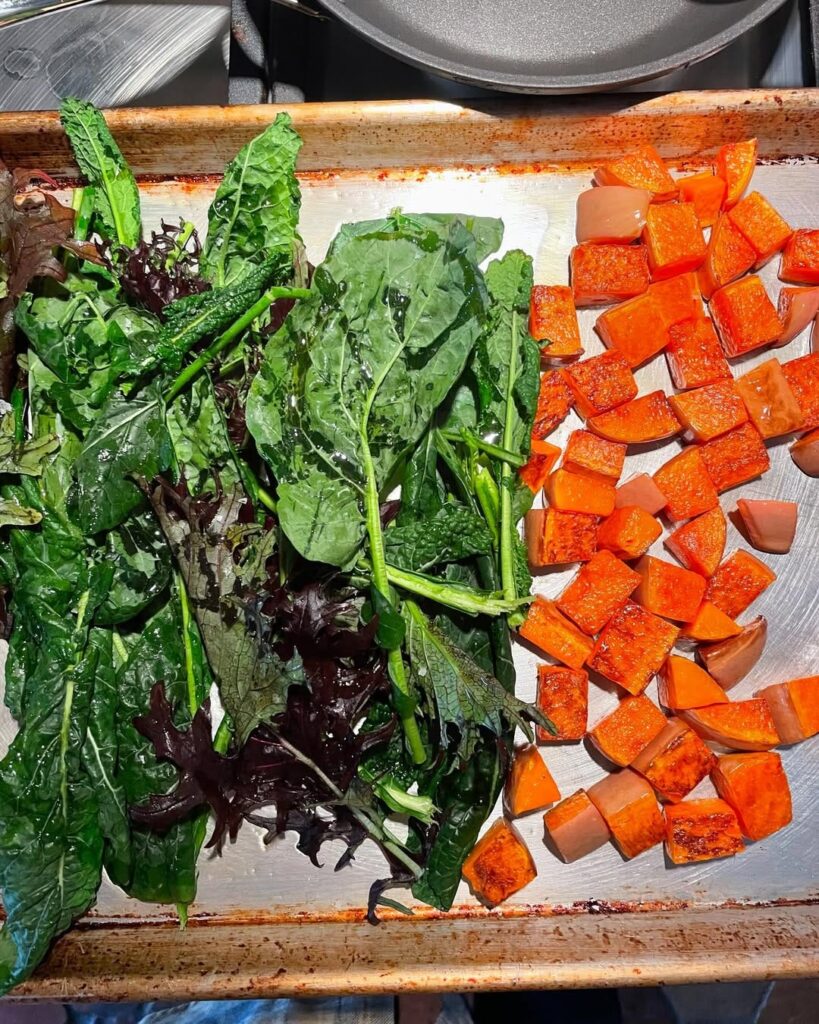 Sheet pan of leafy greens and cubed sweet potatoes ready to roast