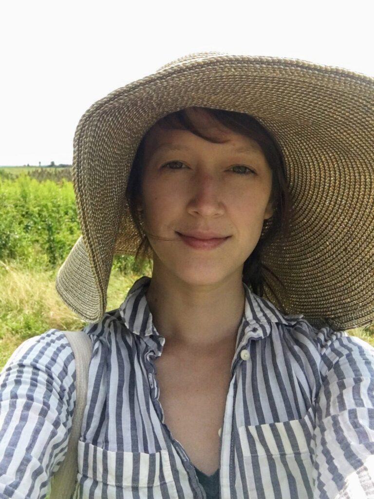 Cathy Erway outdoors in a wide straw sun hat and striped shirt