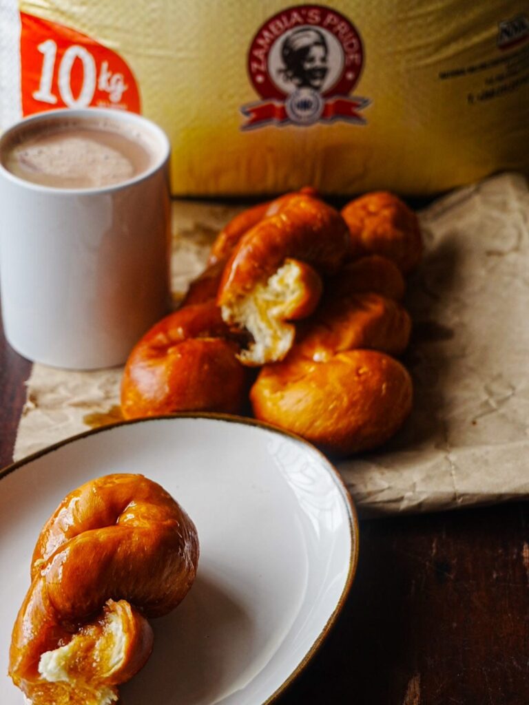 Beautiful twisted doughnuts made with Zambia’s Pride Vitumbuwa Mix on a white plate with a cup of coffee