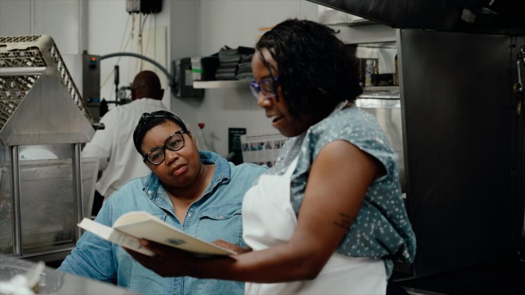 Two Black women reading a cookbook in a commercial kitchen