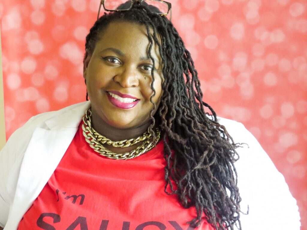 Demetra Overton looking at camera smiling in red shirt and white blazer