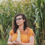 Denise standing in a corn field holding an ear of corn