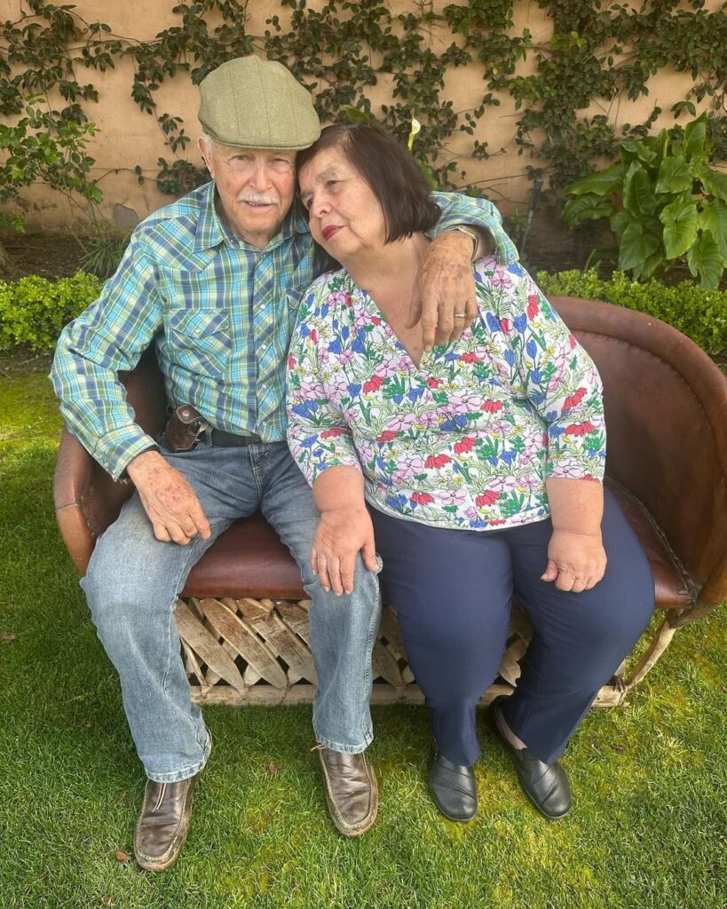Denise’s mom and dad sitting outside on patio furniture, leaning toward one another.