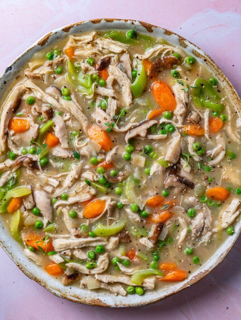 Overhead view of a large dish of shredded chicken stew with peas, carrots, celery and mushrooms