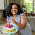 Eden Westbrook standing in her kitchen with a cake topped with strawberries