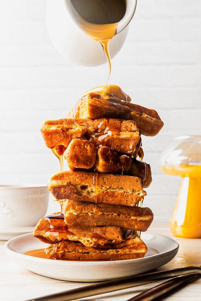 a plate of fluffy waffles with syrup being poured on top