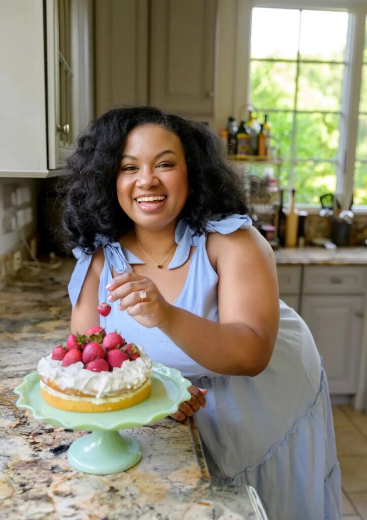 Eden Westbrook standing in her kitchen with a cake topped with strawberries