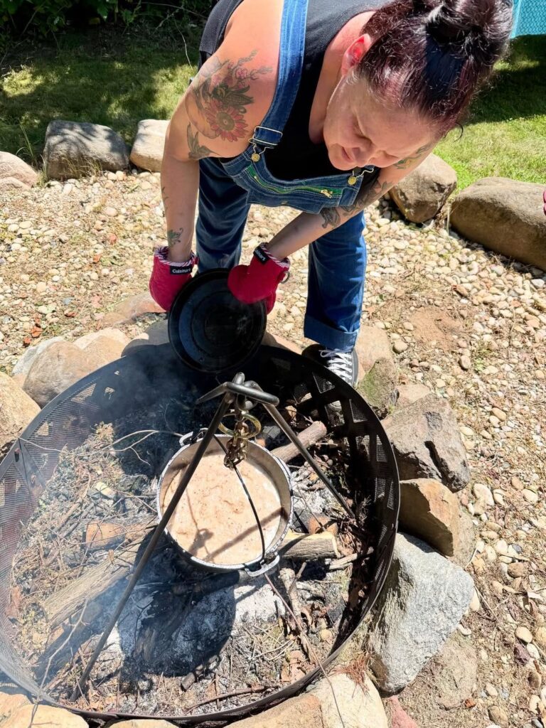 Chef Elena cooking over an open flame with a tripod and a cast iron pot.