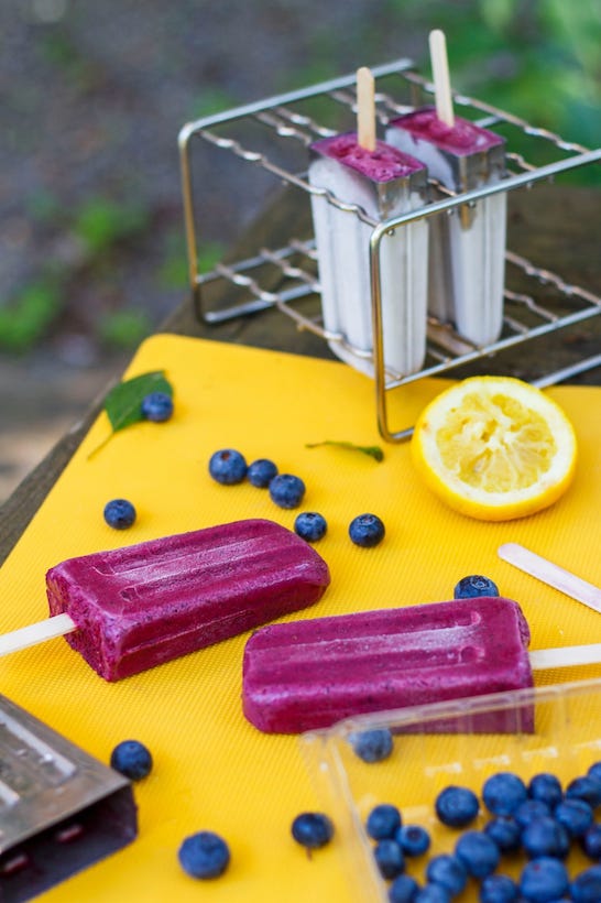Blueberry lemon popsicles on a yellow cutting board with fresh blueberries