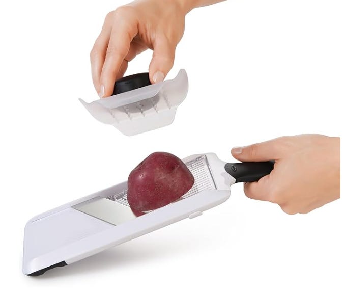 Two hands holding a white mandoline slicer with an apple in the slicer, about the slice
