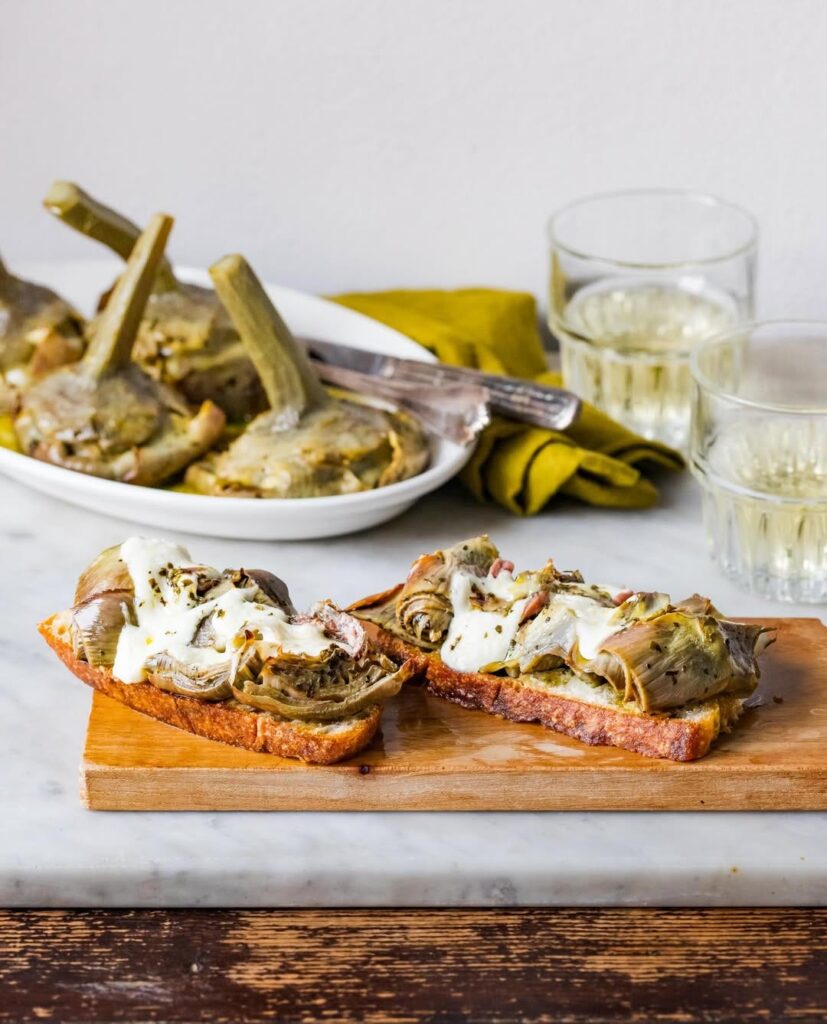 crostini with artichokes on a wooden board and two glasses of wine