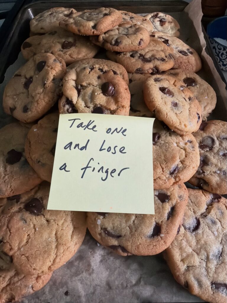 A tray of chocolate chip cookies with a sticky note that reads “Take one and lose a finger”