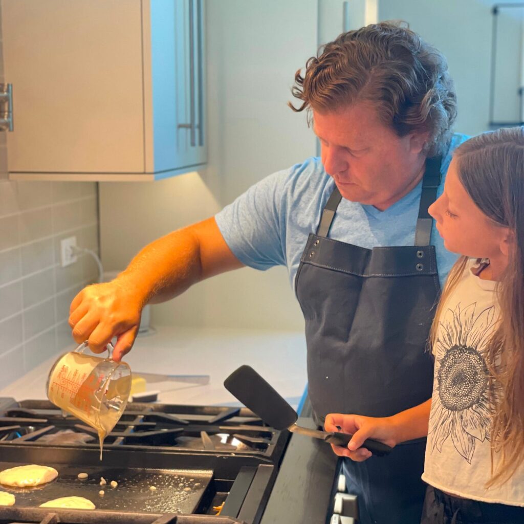 Father and daughter standing at a stovetop making pancakes