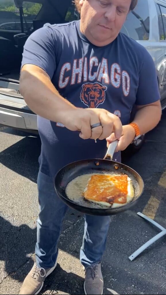 Ted Pappas cooking a grilled sandwich in a pan at a tailgate