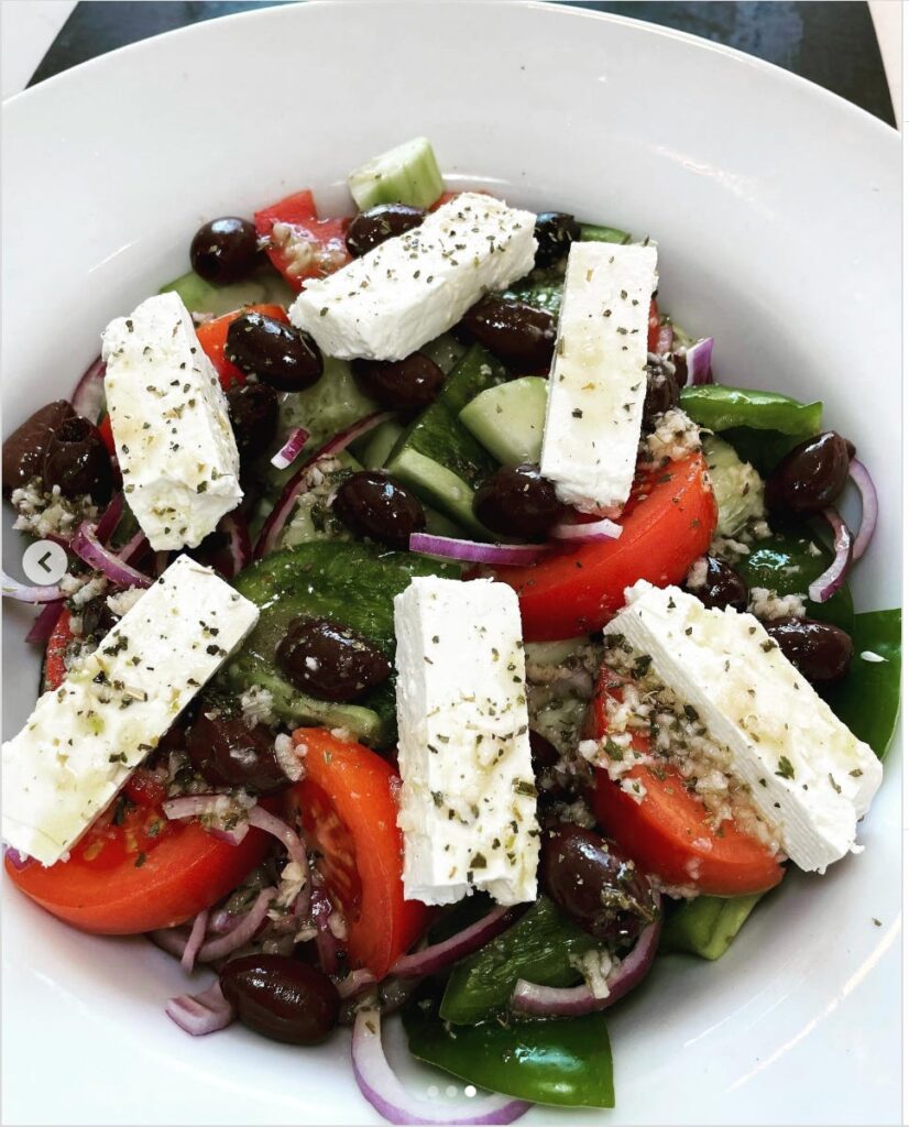 Greek Village Salad in a white bowl - feta cheese, kalamata olives, red onion, green pepper