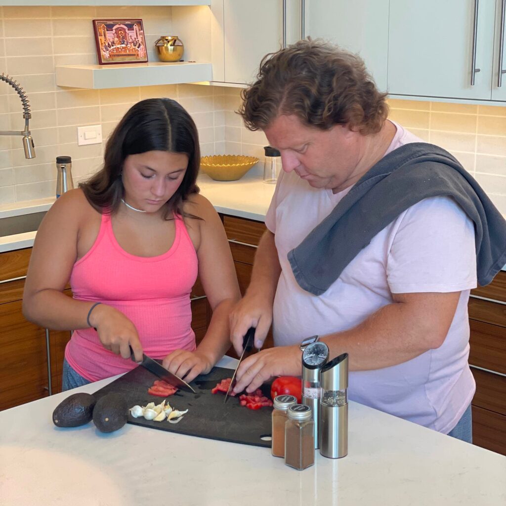 Father and daughter standing at a kitchen counter chopping vegetables